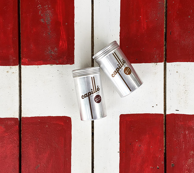 Zwei Dosen des Haarprodukts Camille liegen auf einem Holzbrett, die als Schweizer Flagge bemalt ist