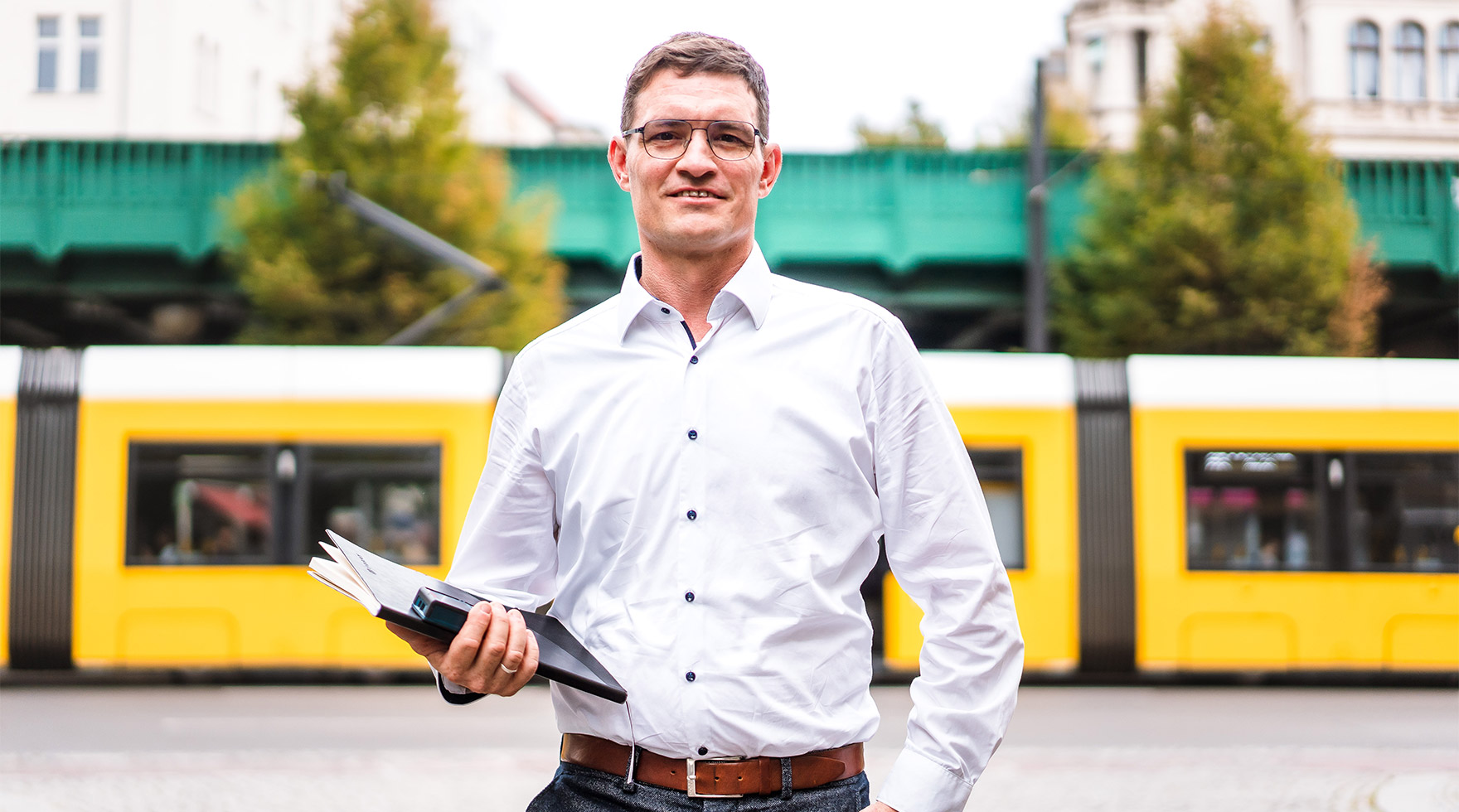 Porträt von Rene Höno des Unternehmens phonux events auf der Straße. Eine Tram fährt hinter ihm lang.