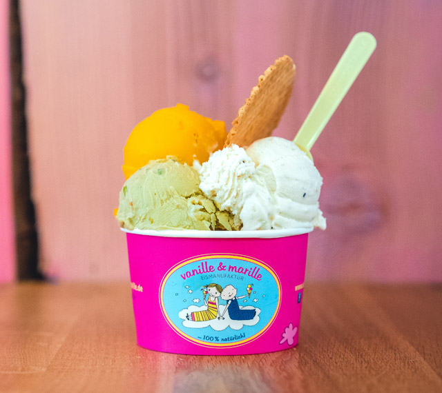 Eisbecher der Eismanufaktur Vanille und Marille mit drei Eiskugeln, einem Löffel und einer Waffel
